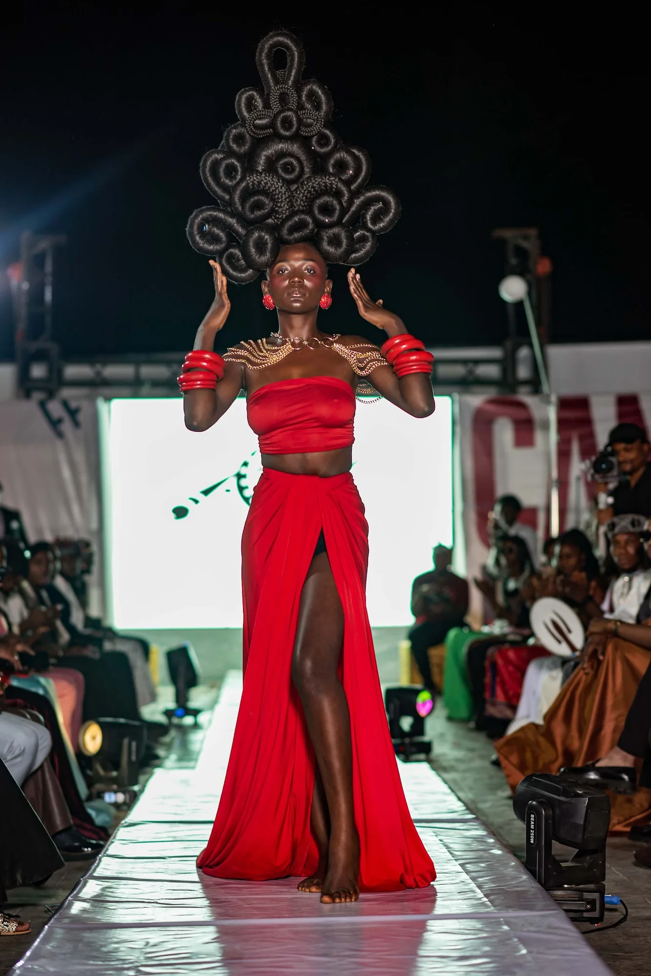 Model in a red gown and sculpted headpiece on the CAMFFEST runway