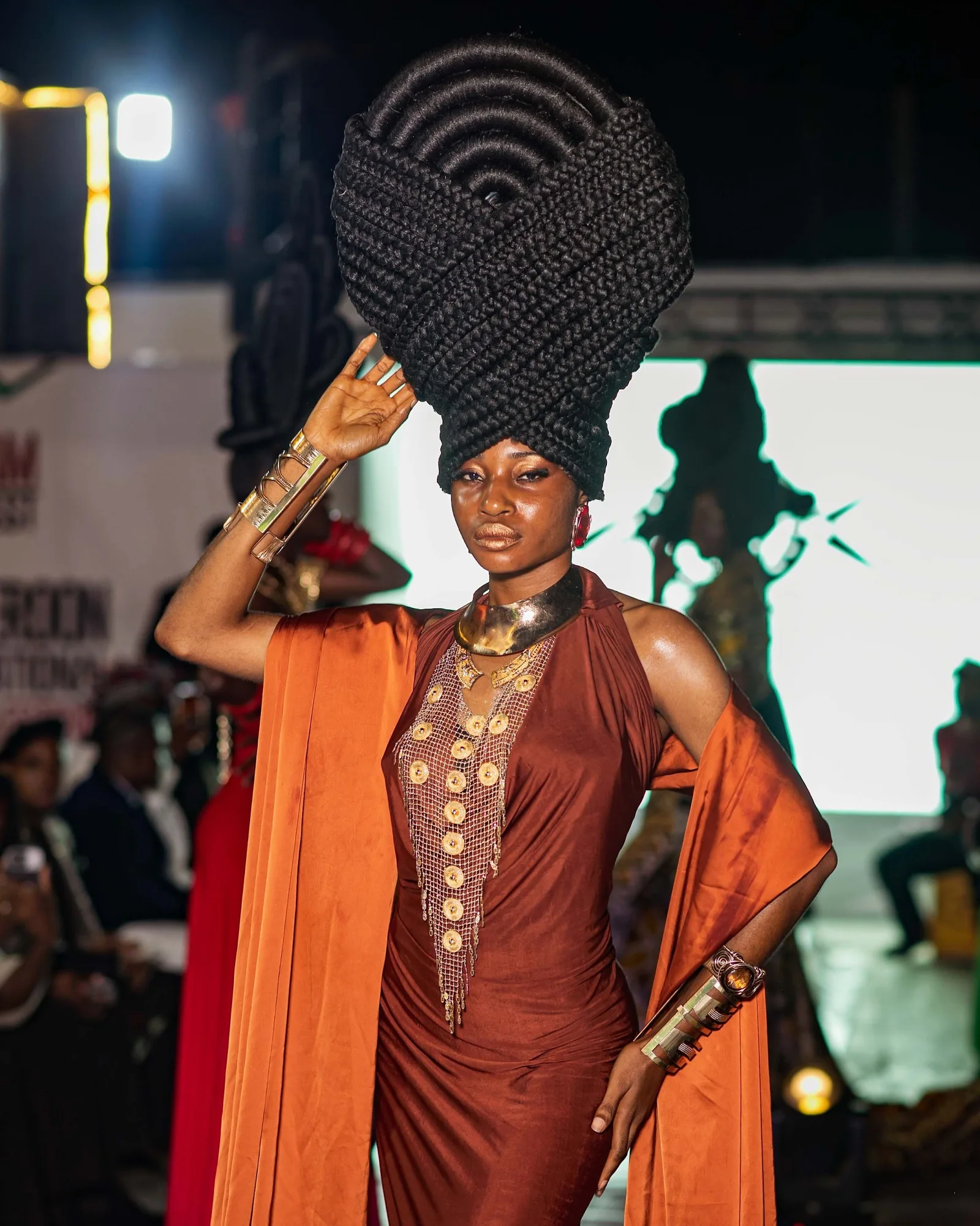 Model in a sculpted headpiece and burnt-orange wrap on the runway
